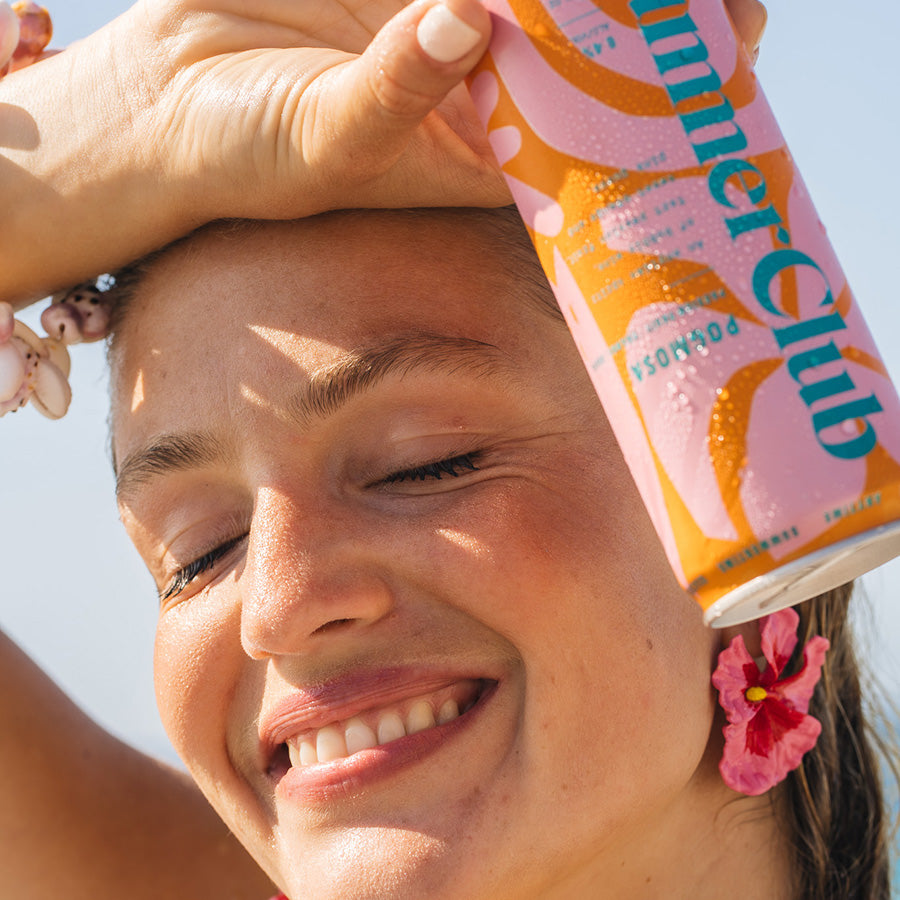 Woman holding a can of Pogmosa up against a clear blue sly.