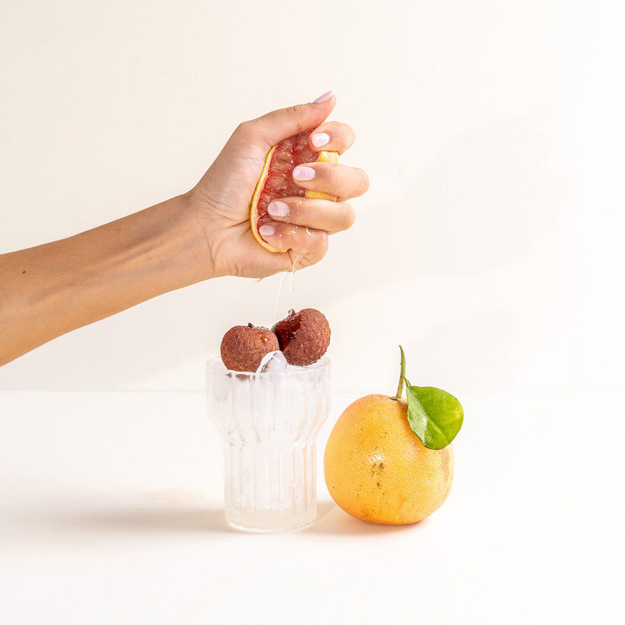 Hand squeezing grapefruit over glass of lychee and ice