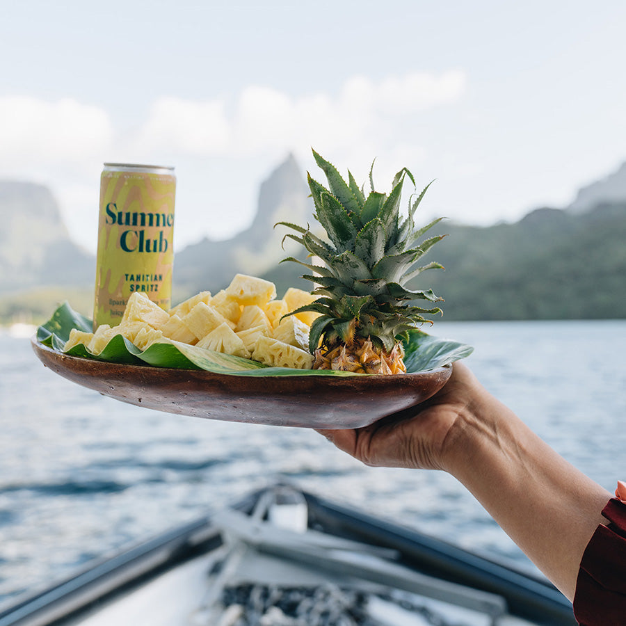 Woman on a boat holding platter of Tahitian Spritz, pineapple chunks, and the top of a pineapple.