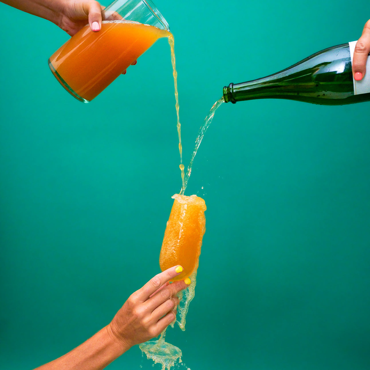 Person pouring orange juice from a bottle into a glass with a green background
